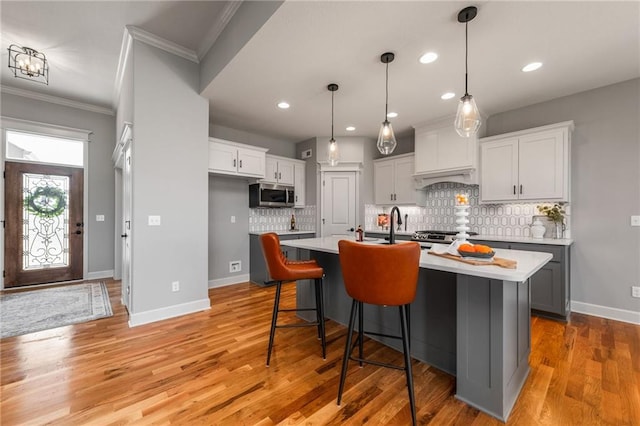 kitchen with a breakfast bar, white cabinetry, decorative light fixtures, a center island with sink, and light hardwood / wood-style floors