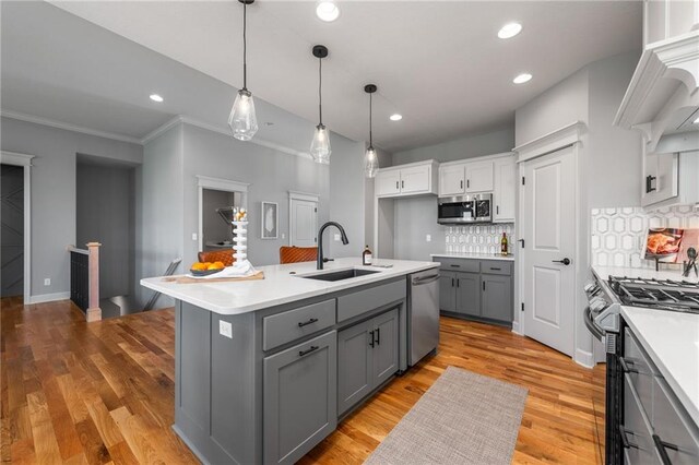 kitchen featuring sink, hanging light fixtures, stainless steel appliances, a kitchen island with sink, and white cabinets