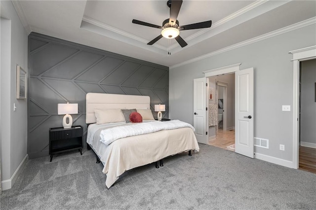 carpeted bedroom with a tray ceiling, ornamental molding, and ceiling fan