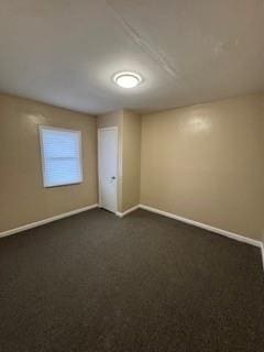 unfurnished room with dark carpet and baseboards