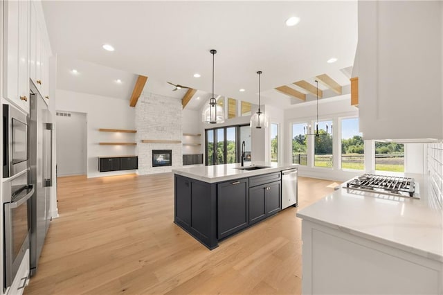 17021 Parkhill St, Overland Park, KS 66221 - kitchen featuring appliances with stainless steel finishes, beamed ceiling, a stone fireplace, light wood-style floors, and white cabinetry