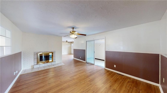 unfurnished living room featuring ceiling fan, a brick fireplace, a textured ceiling, and light hardwood / wood-style flooring