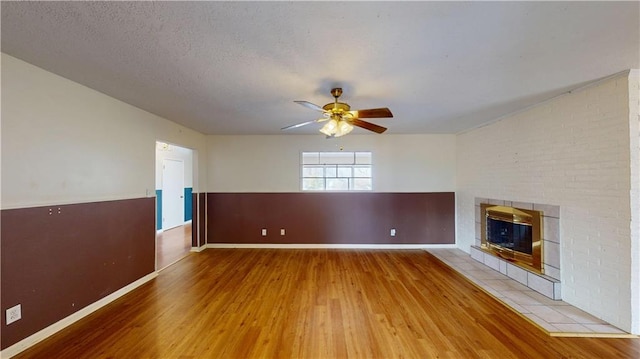 unfurnished living room with a brick fireplace, hardwood / wood-style flooring, a textured ceiling, and ceiling fan