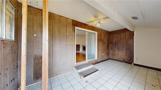 empty room with ceiling fan, vaulted ceiling with beams, light tile patterned floors, and wooden walls