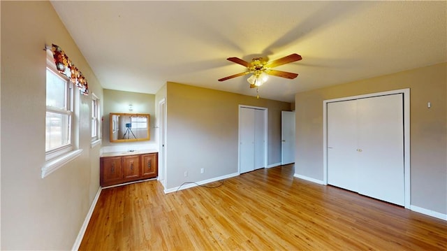 unfurnished bedroom with two closets, light hardwood / wood-style floors, and ceiling fan