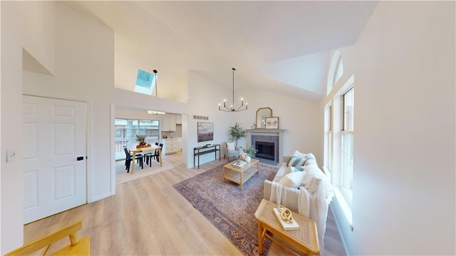 living room with a notable chandelier, high vaulted ceiling, light hardwood / wood-style floors, and a wealth of natural light