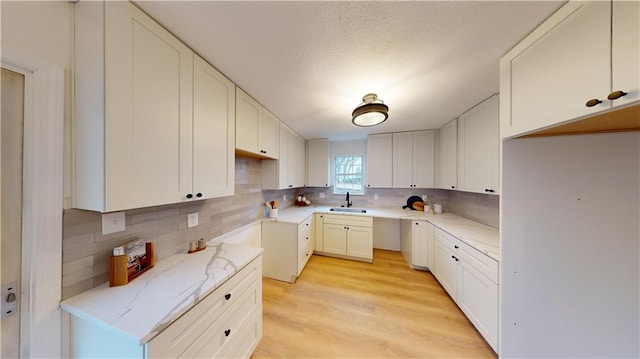 kitchen with tasteful backsplash, sink, white cabinets, light stone countertops, and light hardwood / wood-style flooring