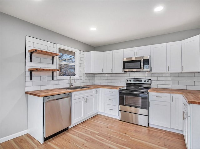 kitchen with butcher block counters, sink, white cabinetry, and stainless steel appliances