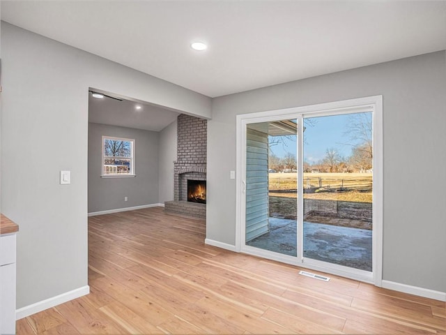 unfurnished living room with a brick fireplace, plenty of natural light, and light wood-type flooring