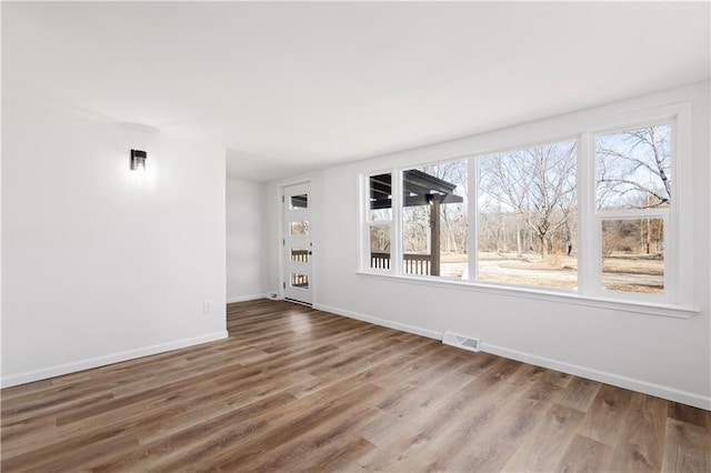 unfurnished room featuring baseboards, visible vents, and wood finished floors