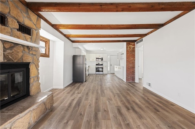 unfurnished living room featuring baseboards, visible vents, wood finished floors, a stone fireplace, and beam ceiling