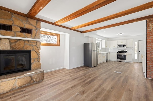 unfurnished living room with light wood-style flooring, a fireplace, visible vents, and beam ceiling