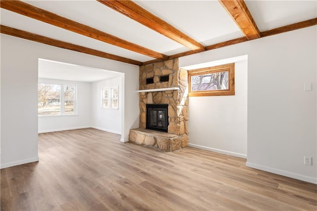 unfurnished living room featuring beamed ceiling, a stone fireplace, baseboards, and wood finished floors