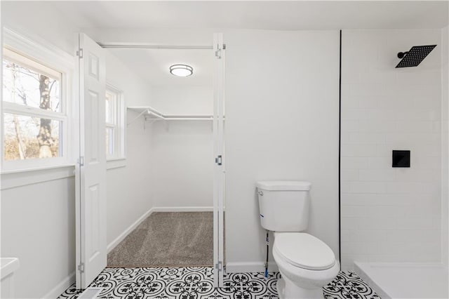 bathroom with toilet, baseboards, a walk in closet, and tiled shower