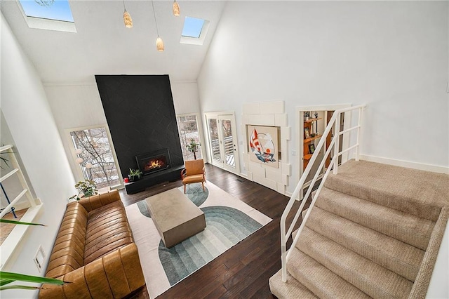 living room with a skylight, a large fireplace, wood finished floors, stairs, and high vaulted ceiling