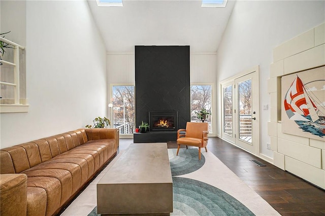 living room featuring a skylight, visible vents, a large fireplace, high vaulted ceiling, and hardwood / wood-style flooring