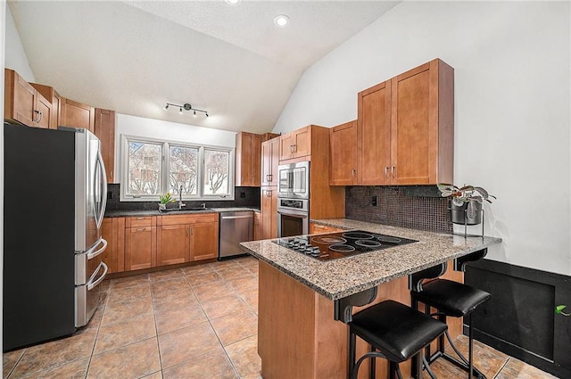 kitchen featuring a breakfast bar area, stainless steel appliances, brown cabinetry, vaulted ceiling, and a peninsula