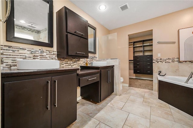 full bathroom with a walk in closet, tasteful backsplash, visible vents, toilet, and vanity