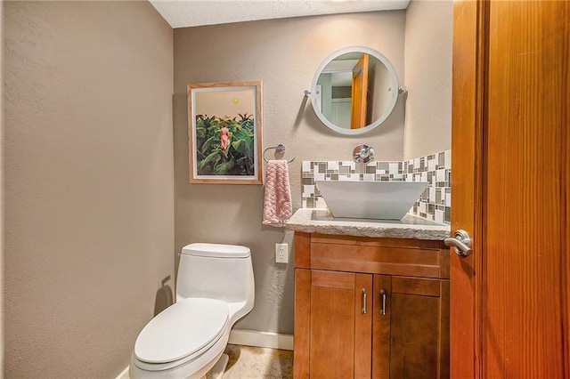 half bath with a textured wall, toilet, backsplash, and vanity