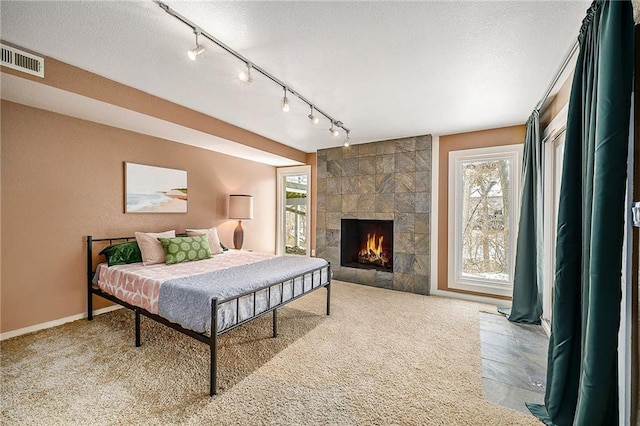 bedroom with a textured ceiling, multiple windows, a tiled fireplace, and visible vents