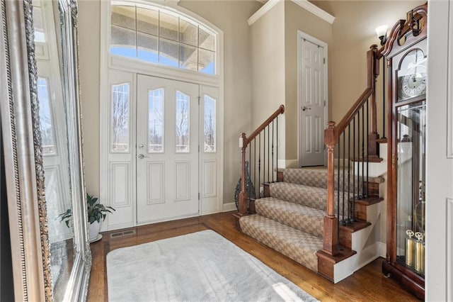 foyer entrance with baseboards, stairs, visible vents, and wood finished floors