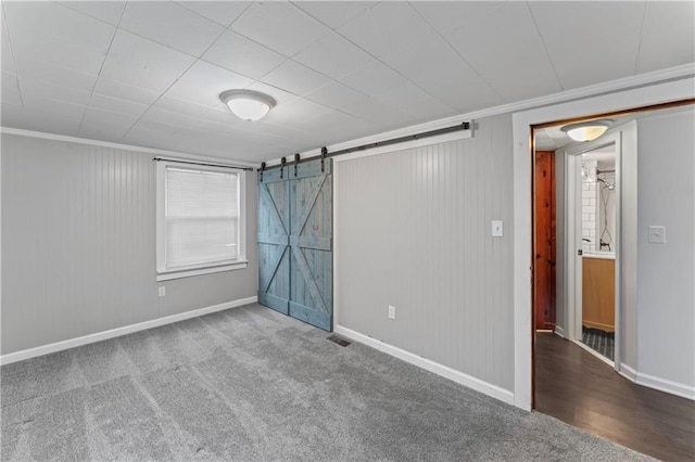 empty room featuring visible vents, a barn door, baseboards, ornamental molding, and carpet flooring