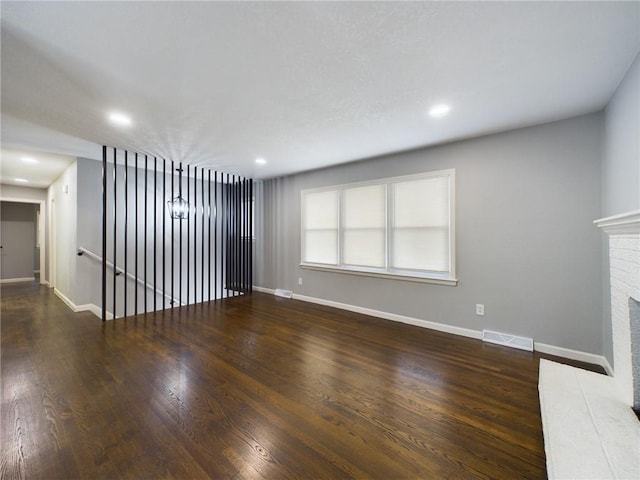 unfurnished living room with a brick fireplace and dark wood-type flooring