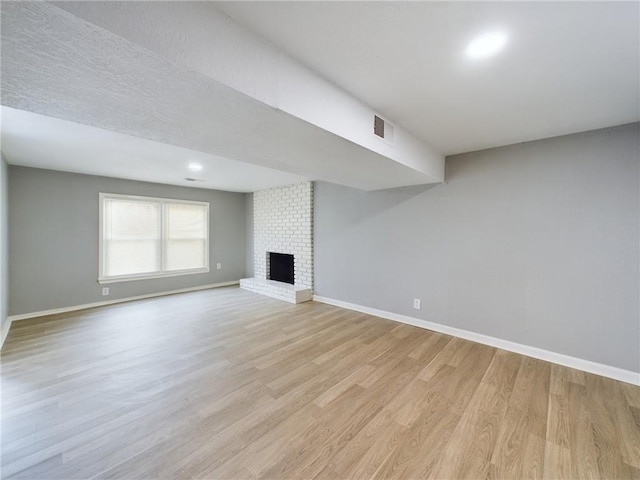 unfurnished living room with a brick fireplace, light hardwood / wood-style flooring, and a textured ceiling