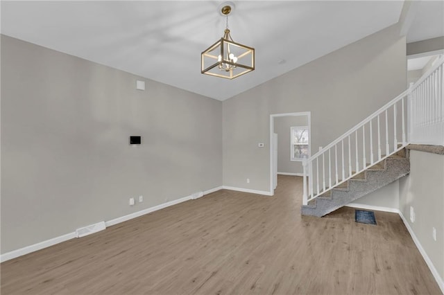 unfurnished living room featuring lofted ceiling, wood-type flooring, and a notable chandelier