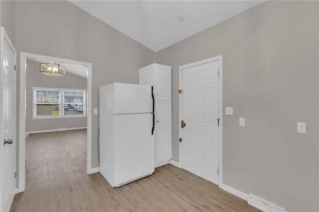 kitchen with white refrigerator, lofted ceiling, an inviting chandelier, and light wood-type flooring