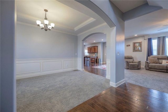 interior space featuring dark colored carpet, a wainscoted wall, crown molding, and arched walkways