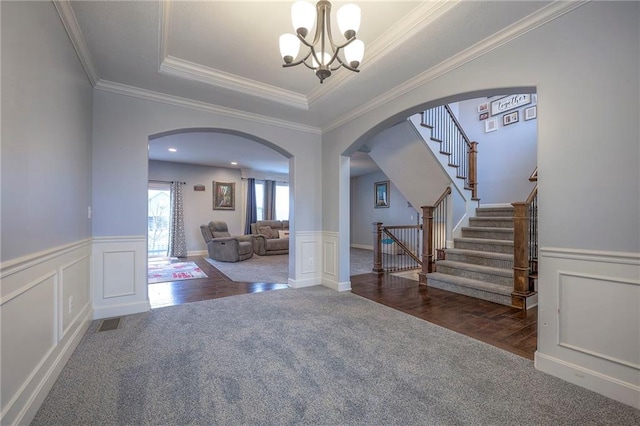 carpeted entrance foyer featuring a raised ceiling, crown molding, and an inviting chandelier