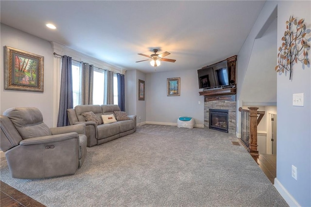 carpeted living area with baseboards, a ceiling fan, and a glass covered fireplace