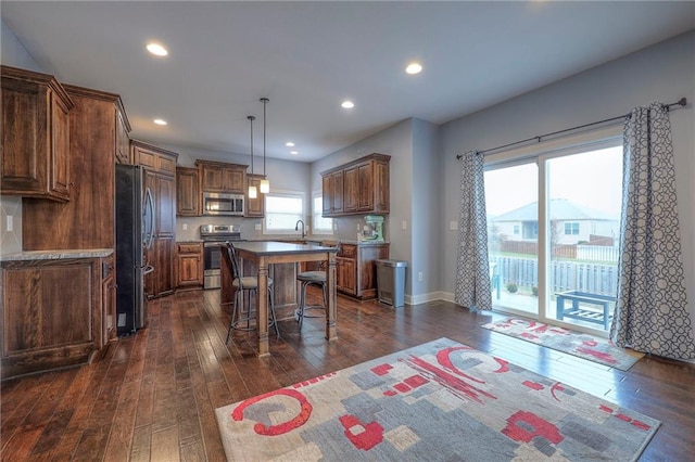 kitchen featuring a kitchen island, dark hardwood / wood-style floors, a breakfast bar, decorative light fixtures, and stainless steel appliances