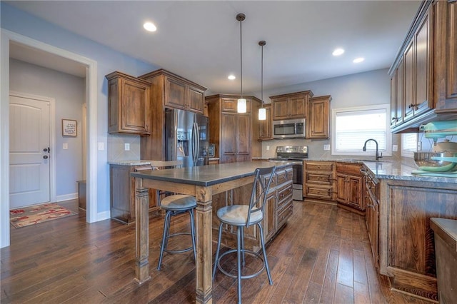 kitchen with dark wood-style flooring, decorative light fixtures, stainless steel appliances, a kitchen island, and a sink