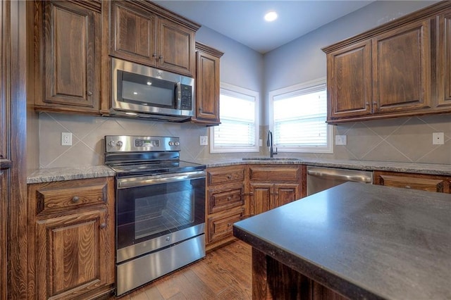 kitchen with stainless steel appliances, light hardwood / wood-style floors, sink, and backsplash