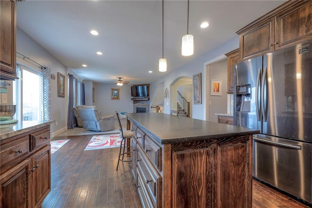 kitchen featuring stainless steel fridge with ice dispenser, a kitchen island, open floor plan, hanging light fixtures, and a stone fireplace