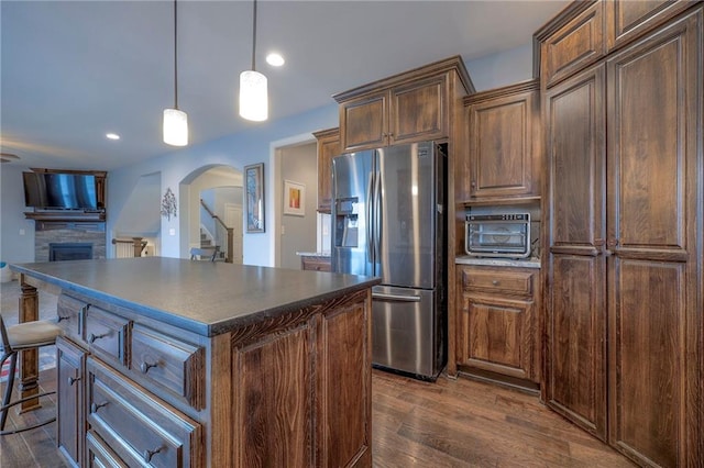 kitchen with stainless steel fridge, dark countertops, a kitchen island, a kitchen breakfast bar, and decorative light fixtures