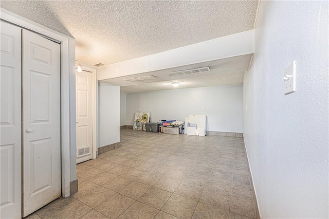 finished basement featuring visible vents, baseboards, and a textured ceiling