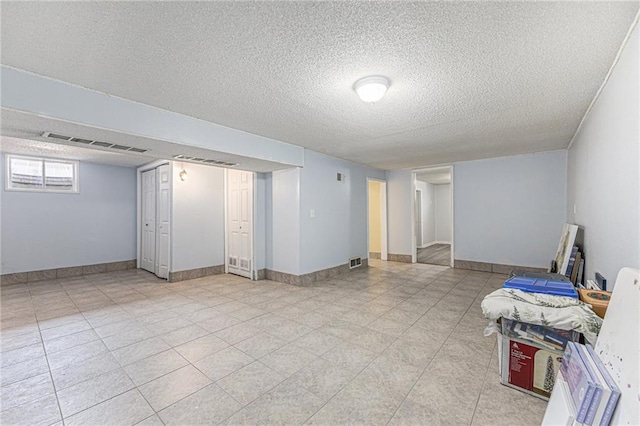 basement featuring visible vents, baseboards, and a textured ceiling