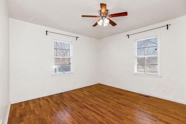 unfurnished room featuring a healthy amount of sunlight, visible vents, and hardwood / wood-style flooring