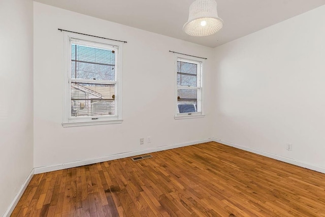 empty room with plenty of natural light, wood-type flooring, visible vents, and baseboards