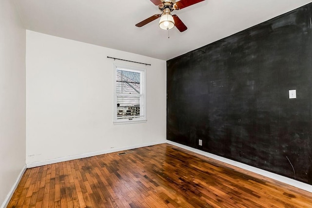 spare room with visible vents, hardwood / wood-style floors, a ceiling fan, an accent wall, and baseboards