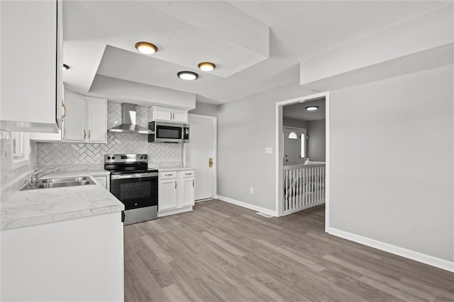 kitchen featuring a sink, wall chimney range hood, backsplash, stainless steel appliances, and light countertops