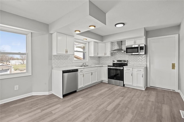 kitchen featuring light wood-style flooring, wall chimney range hood, white cabinetry, stainless steel appliances, and light countertops