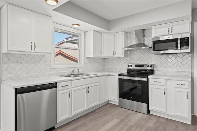 kitchen featuring a sink, light wood-style floors, appliances with stainless steel finishes, white cabinetry, and wall chimney exhaust hood