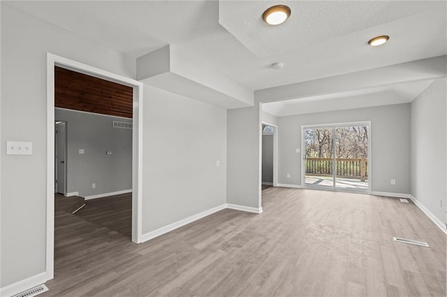 empty room with visible vents, wood finished floors, baseboards, and a textured ceiling