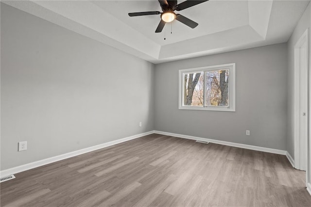 empty room with a raised ceiling, wood finished floors, and baseboards