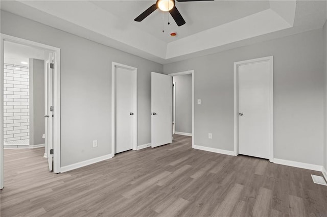 unfurnished bedroom with ceiling fan, baseboards, ensuite bathroom, wood finished floors, and a raised ceiling