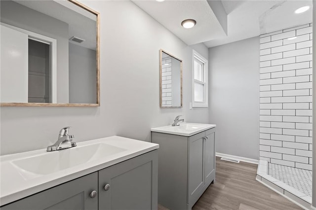 full bathroom with two vanities, wood finished floors, visible vents, and a sink